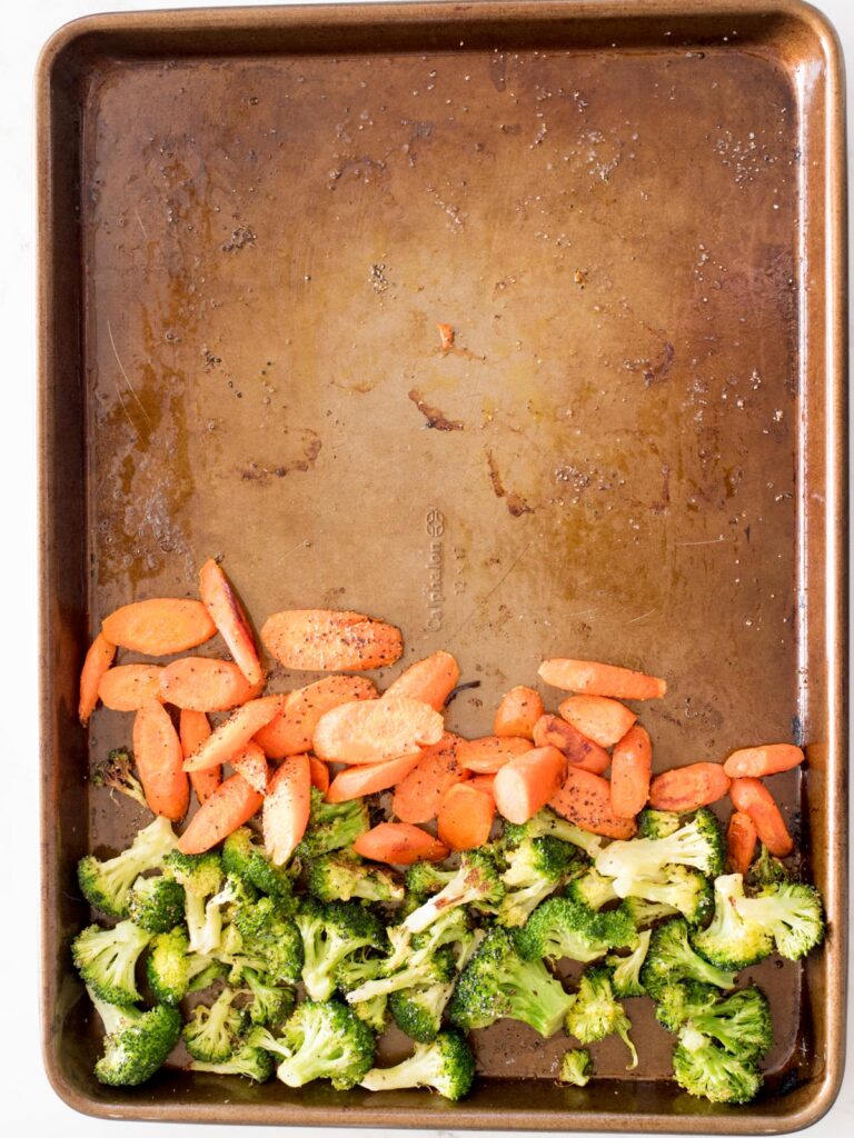 sheet pan with partially roasted broccoli and carrots moved to one side
