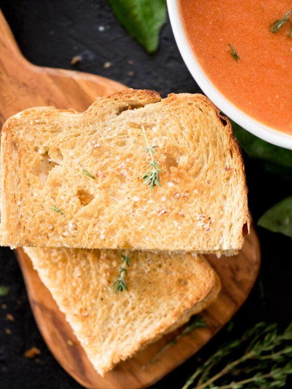 air fried grilled cheese sandwich sliced in half on a cutting board next to a bowl of soup and topped with a sprig of fresh thyme