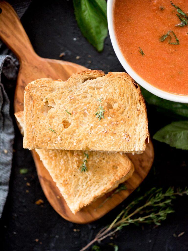air fried grilled cheese sandwich cut in half next to a bowl of tomato basil soup and topped with a small sprig of thyme