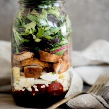 cobb style mason jar salad with lid on and a fork sitting next to it