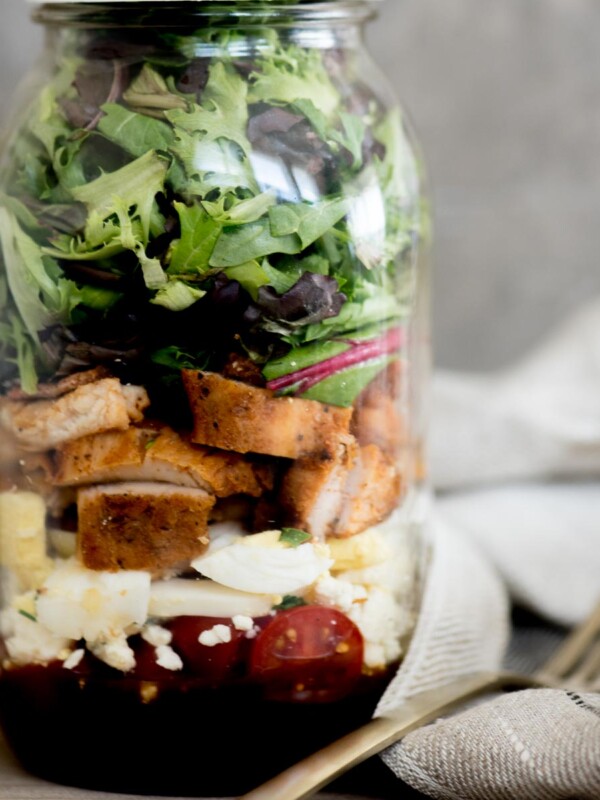 cobb style mason jar salad with lid on and a fork sitting next to it