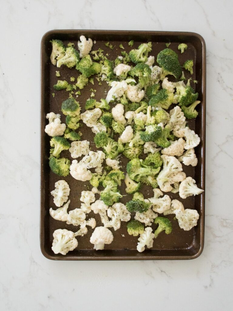 broccoli and cauliflower on a sheet pan seasoned with salt and pepper