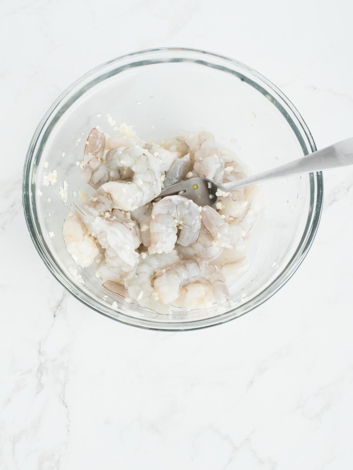 raw shrimp tossed with minced garlic and white wine in a mixing bowl for baked shrimp scampi