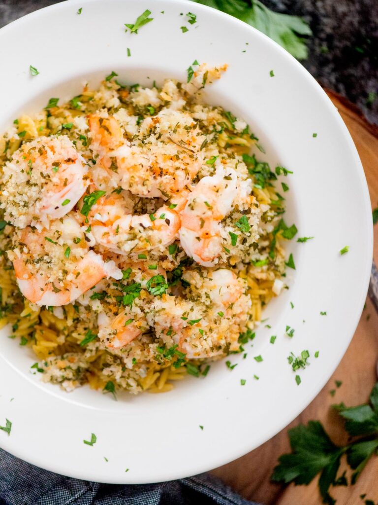 baked shrimp scampi in a bowl on top of orzo pasta and sprinkled with parsley