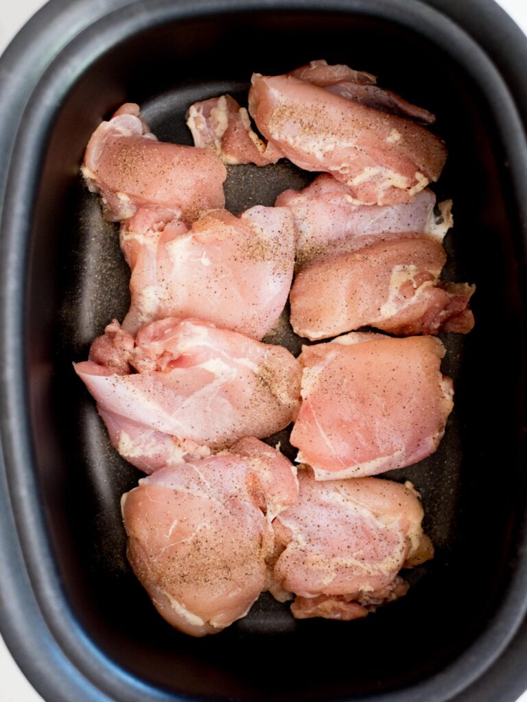 chicken thighs in a crockpot seasoned with salt and pepper