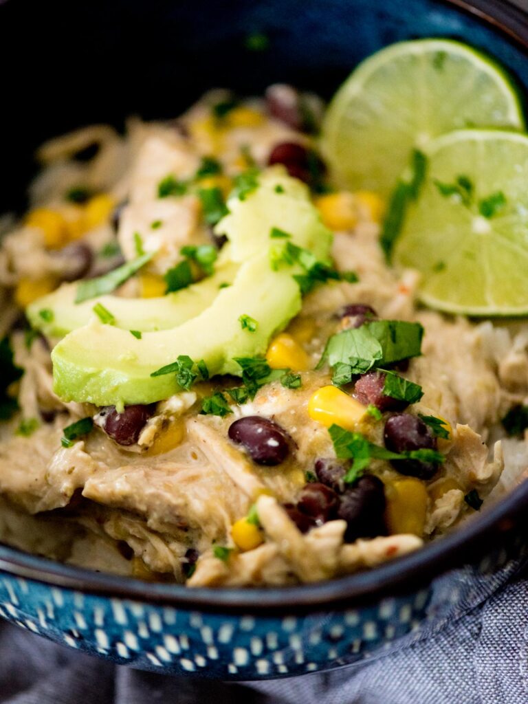 Salsa verde chicken in a bowl over rice topped with avocado and lime.