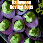 A platter of halloween deviled eggs features purple-tinted whites and bright green filling, labeled Halloween Deviled Eggs on a black background with festive decorations.
