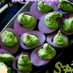 A platter of Halloween deviled eggs featuring purple-dyed whites and green filling, accented by decorative spider and pumpkin graphics.