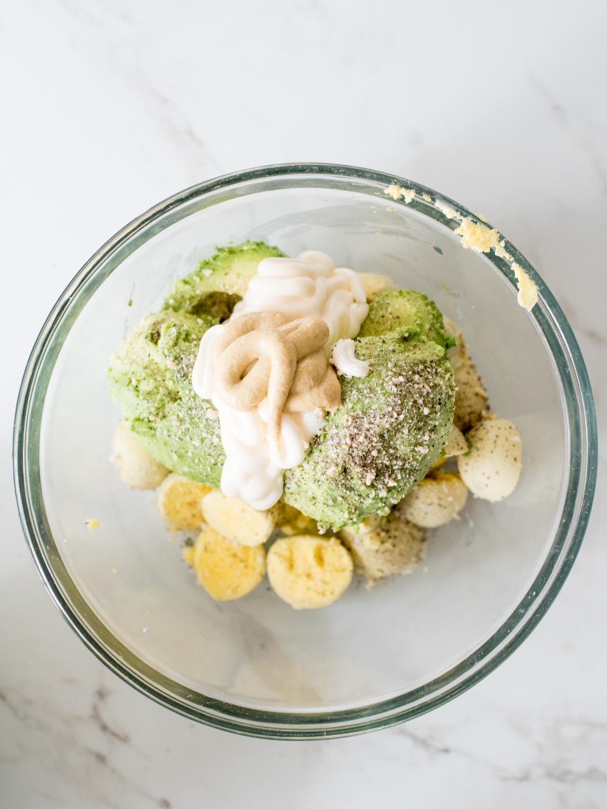 dijon mustard added to mixing bowl with avocado, mayo, seasonings, and yolks