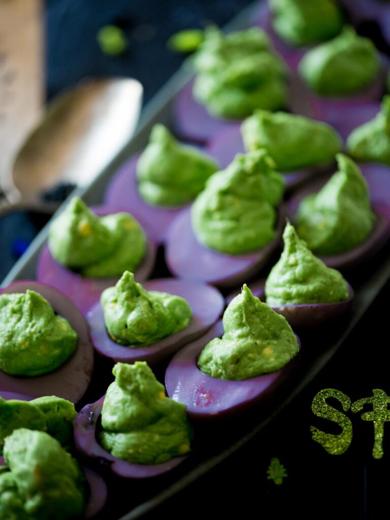 green and purple halloween deviled eggs on a platter