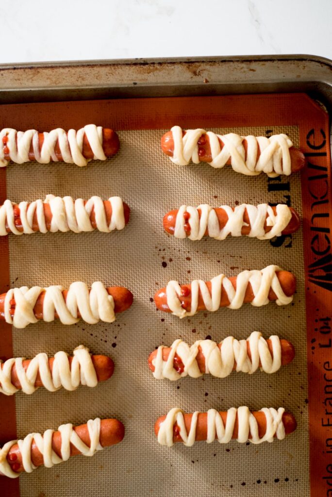 mummy pigs in a blanket on a baking sheet