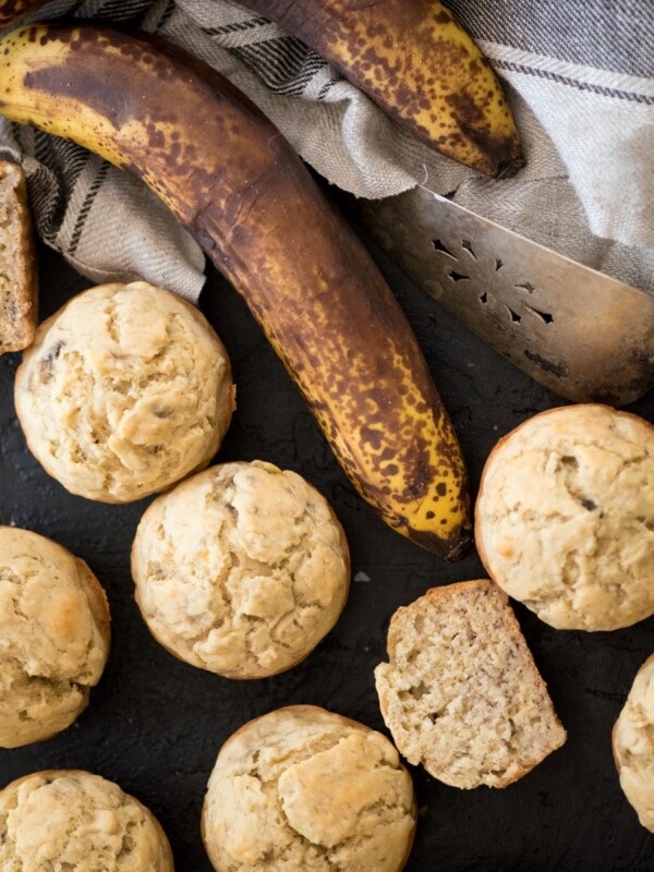 banana muffins with one cut in half, browned bananas, and a tea towel