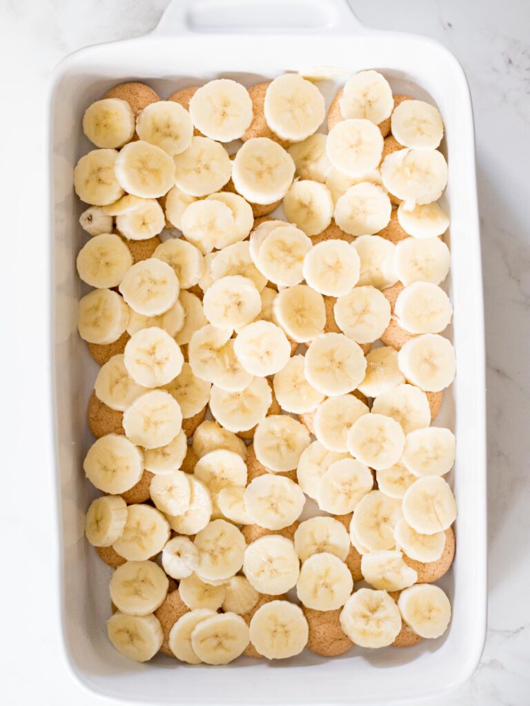 sliced bananas on top of the vanilla wafers in a casserole dish