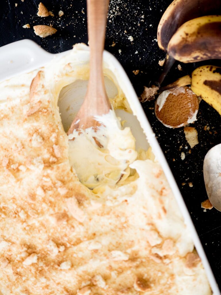 banana pudding being scooped from a casserole dish