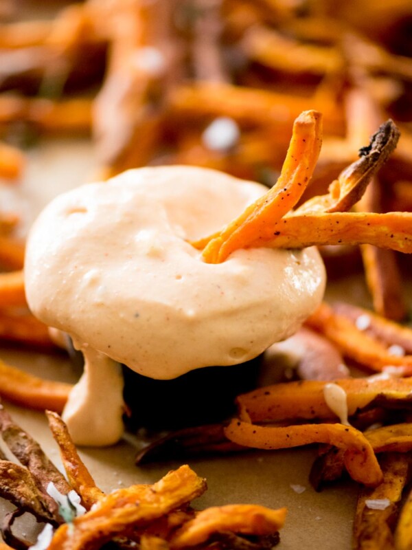 sweet potato fries dipping sauce with surrounded by sweet potatoes and some being dipped in it