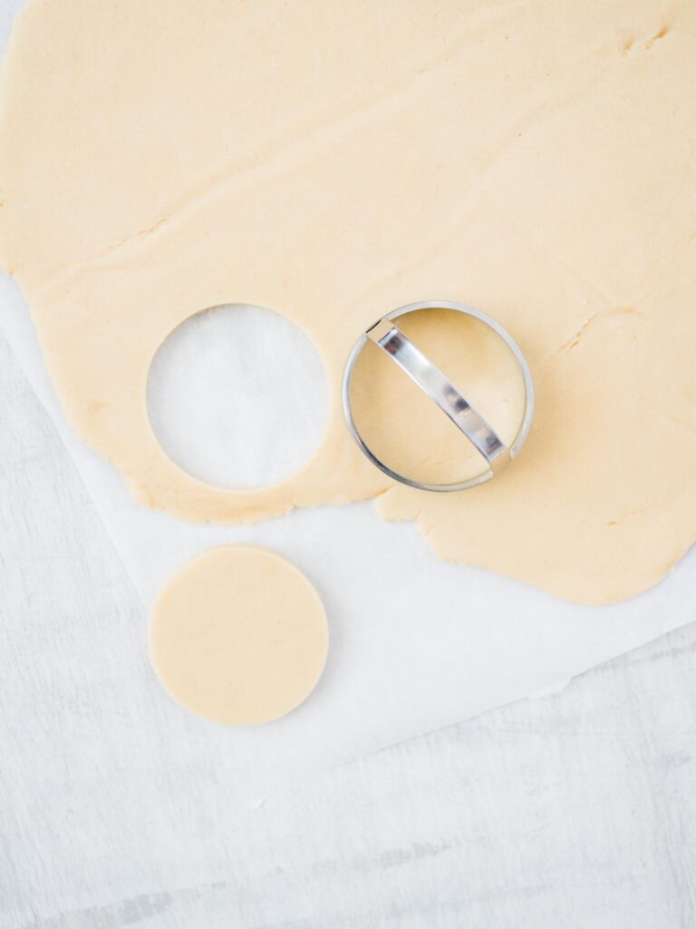 sugar cookie dough being cut out with a circle cookie cutter