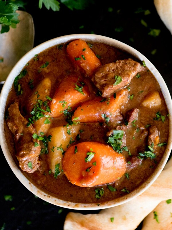 beef stew in a bowl topped with parsley and a side of breadsticks