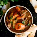 beef stew in a bowl served with breadsticks and topped with parsley