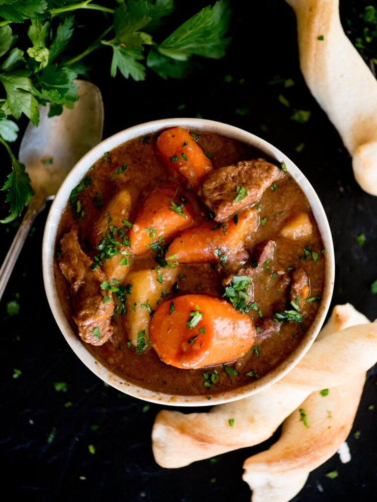 beef stew in a bowl served with breadsticks and topped with parsley
