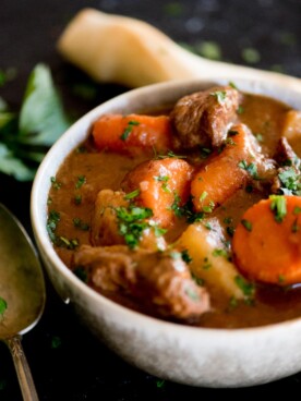 classic beef stew served in a bowl topped with parsley and breadsticks
