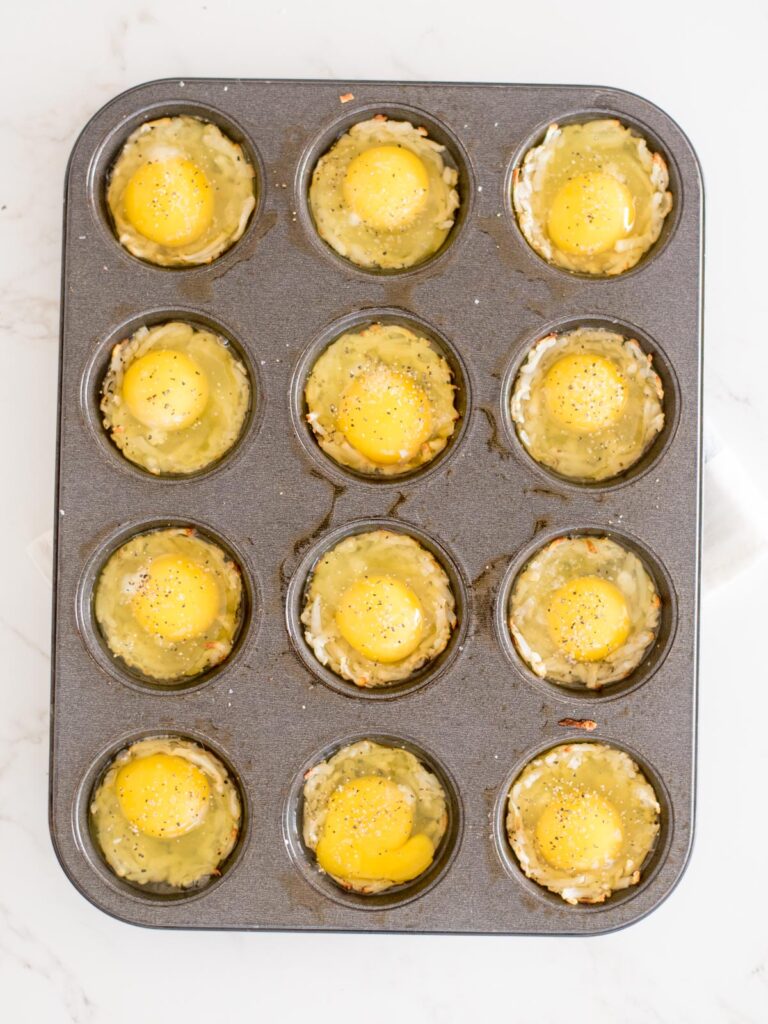 eggs and seasoning added to hashbrowns in a muffin to make eggs in a basket in the oven