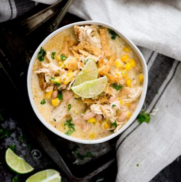 instant pot white chicken chili in a bowl topped with cheese, tortilla strips, limes, and cilantro