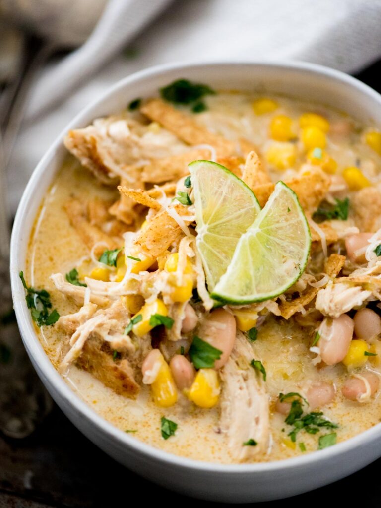 white chicken chili in a bowl topped with cilantro, lime, cheese, and tortilla strips