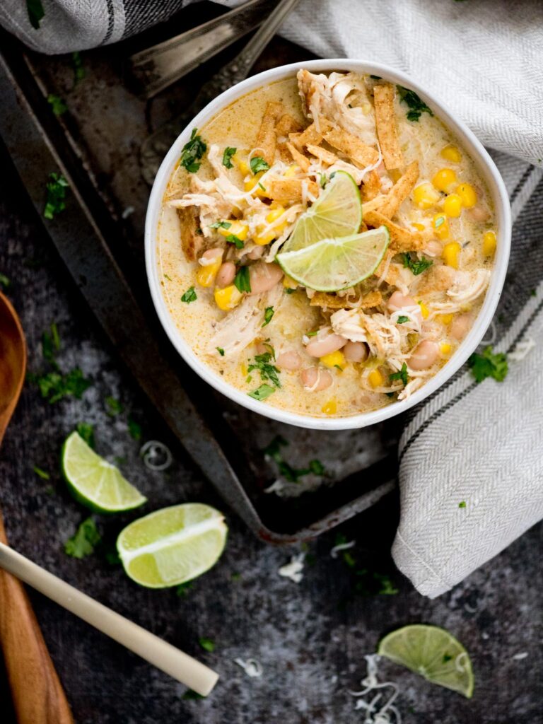 instant pot white chicken chili in a bowl topped with cheese, tortilla strips, and lime