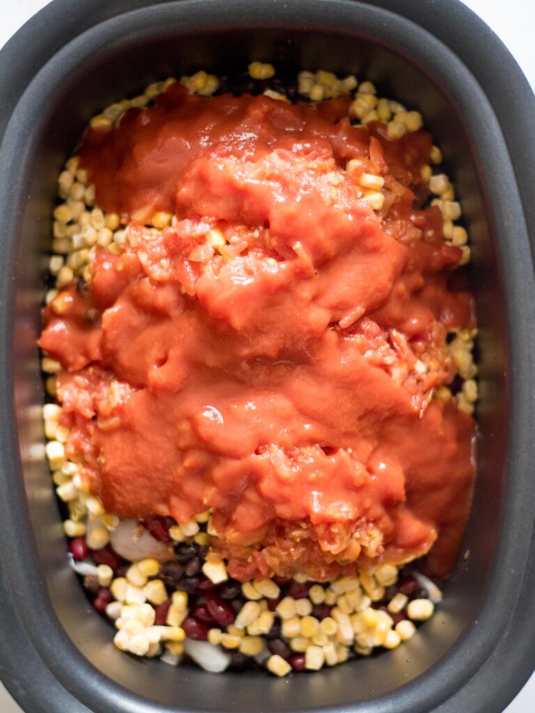 tomato sauce added to seasoned chicken beans and rice in a crockpot