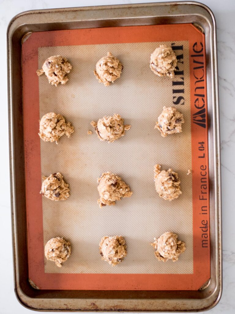 oatmeal raisin cookie dough scooped onto a baking sheet with a silicon baking mat