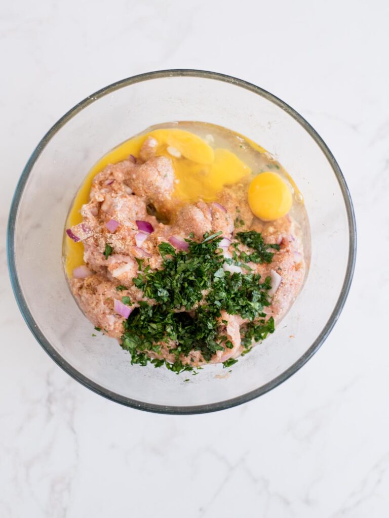 eggs and fresh herbs added to turkey meatball mixture in a mixing bowl