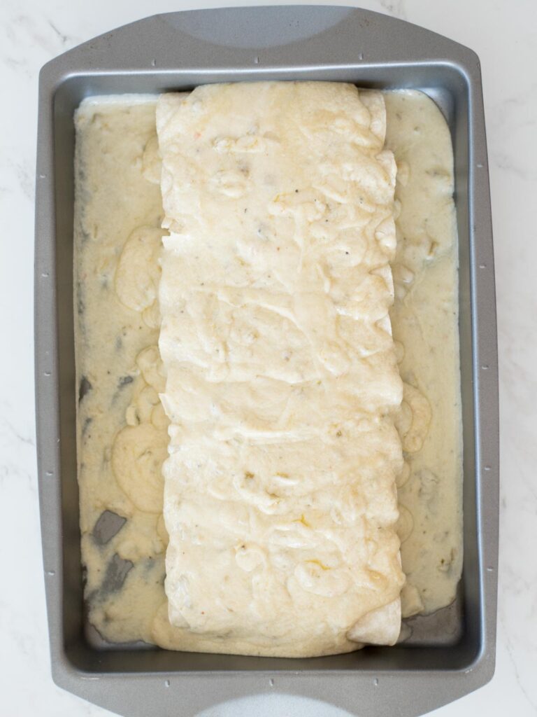 enchiladas topped with sauce in the baking pan