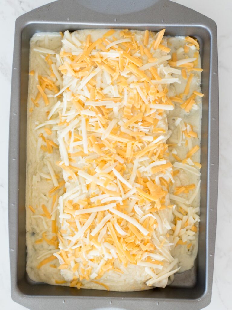 shredded cheese on top of sauced enchiladas
