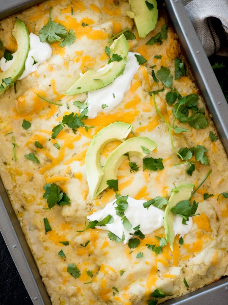 green chile chicken enchiladas topped with sour cream, cilantro, and avocado