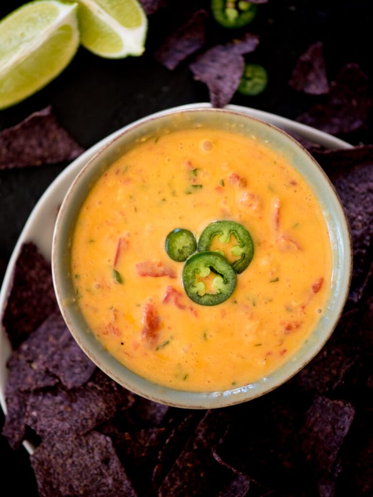 smoked queso in a bowl topped with sliced jalapenos and a chip