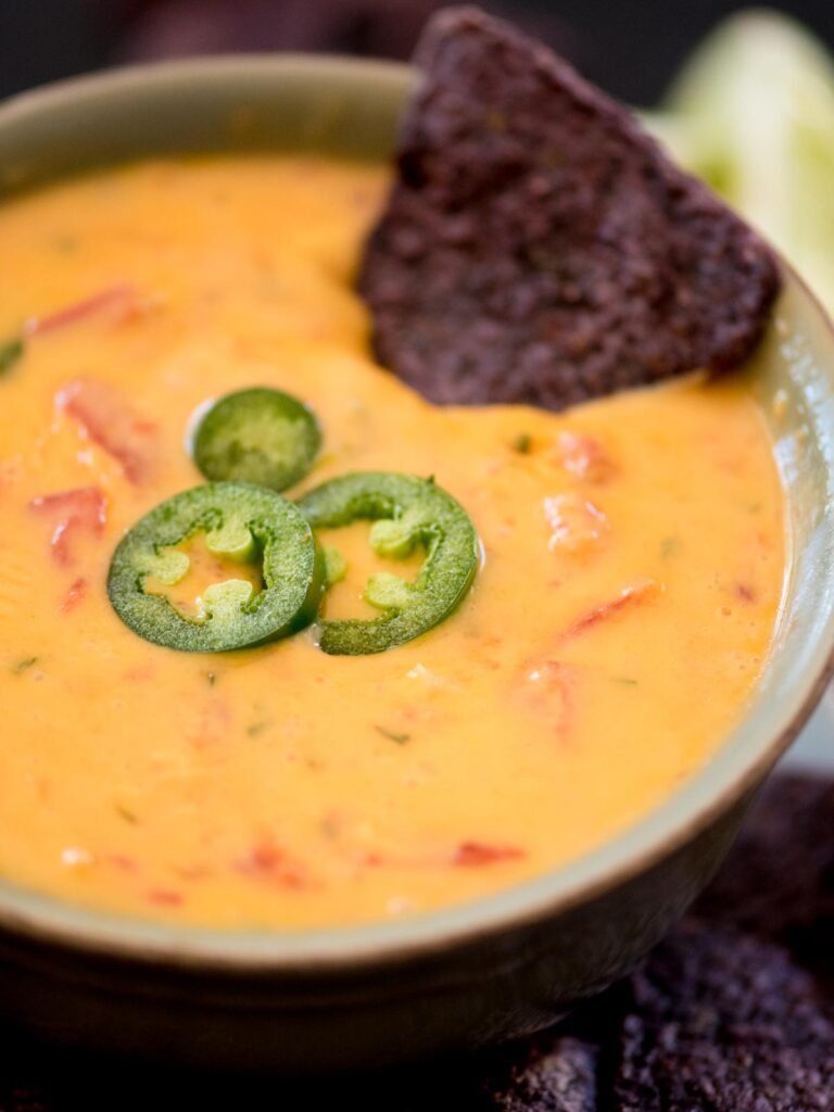 smoked queso in a bowl with jalapeno slices and a chip