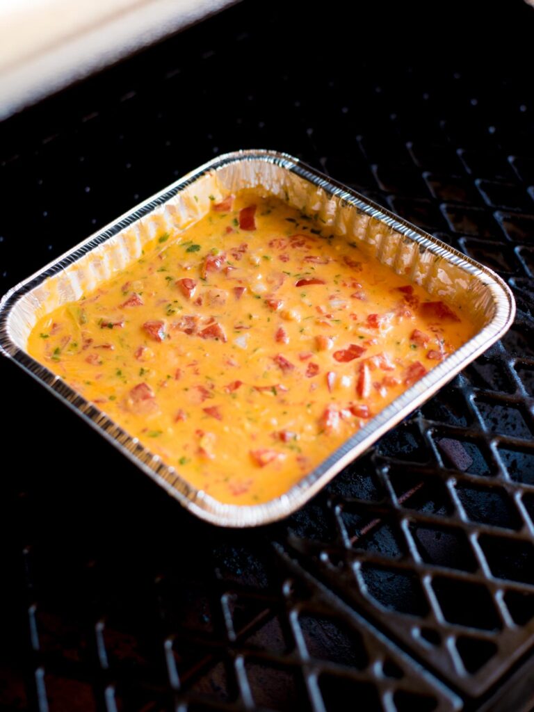smoked queso dip in aluminum pan that has been melted and stirred