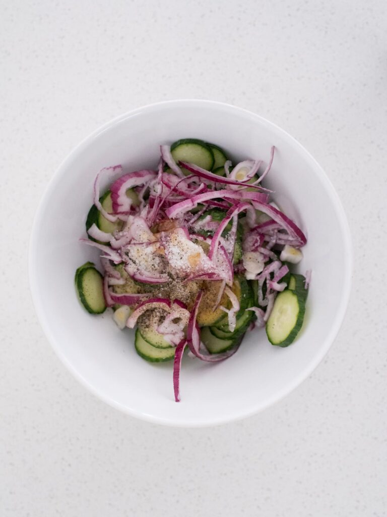 seasonings added to the mixing bowl with cucumbers and red onion