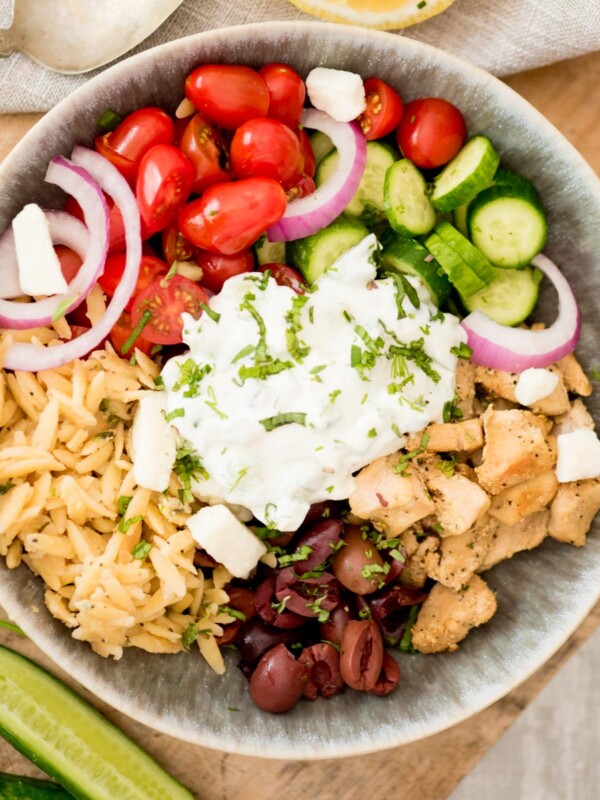 greek chicken bowl surrounded by cucumbers and dill