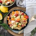greek orzo salad in a bowl topped with fresh dill and surrounded by lemons and dill