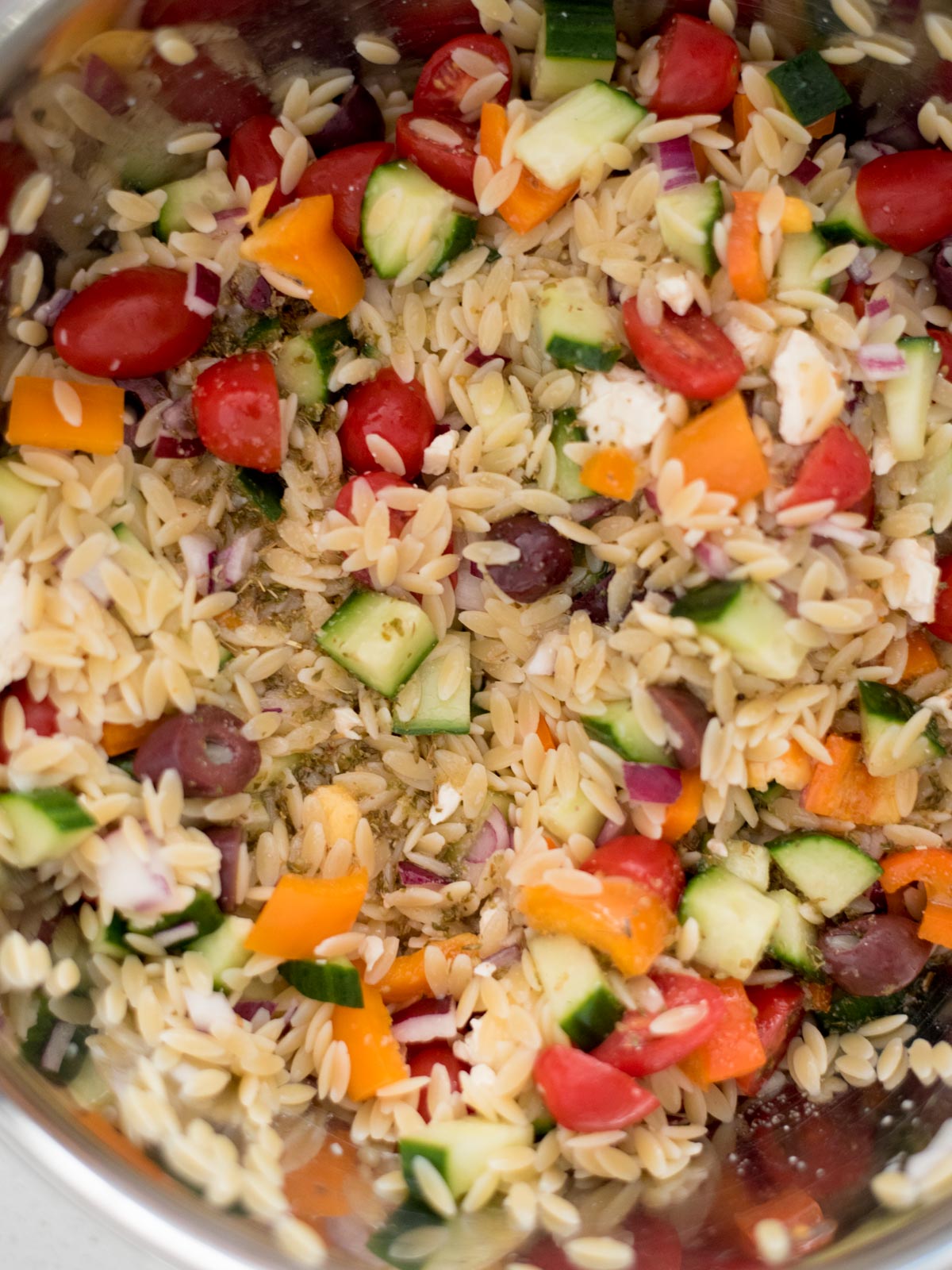 dressing added to orzo and vegetables in a mixing bowl