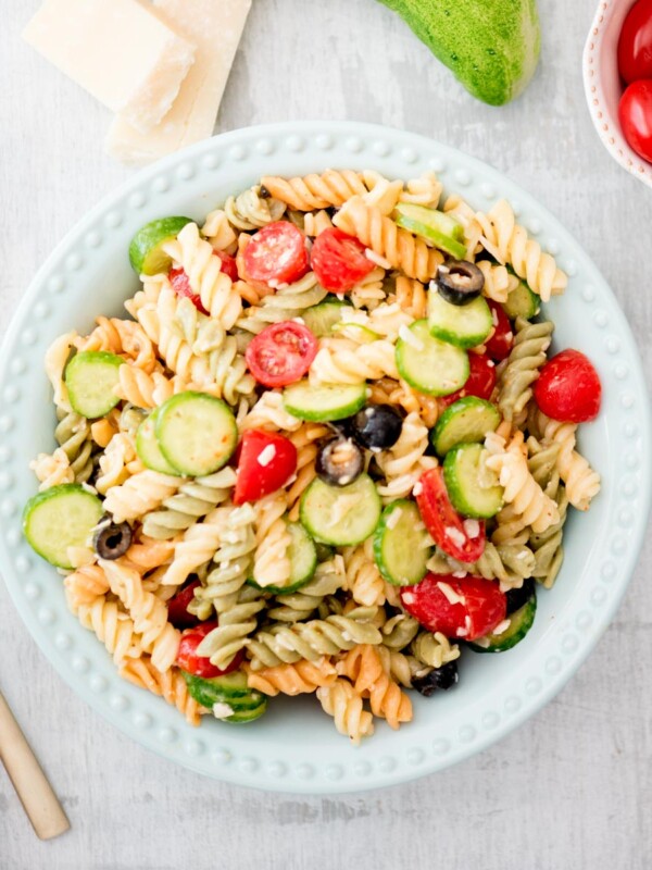 italian pasta salad in a bowl surrounded by parmesan, cucumber, and tomato
