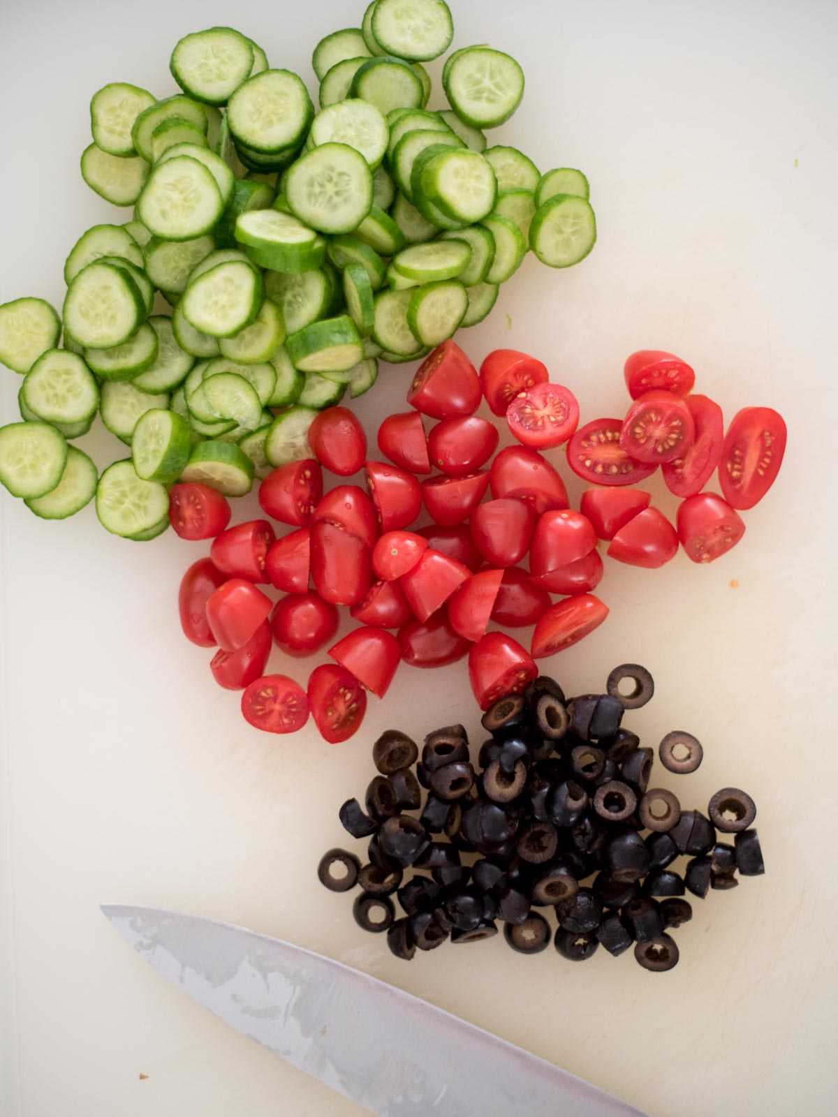 chopped cucumber, olives, and tomatoes on a cutting board with a knife