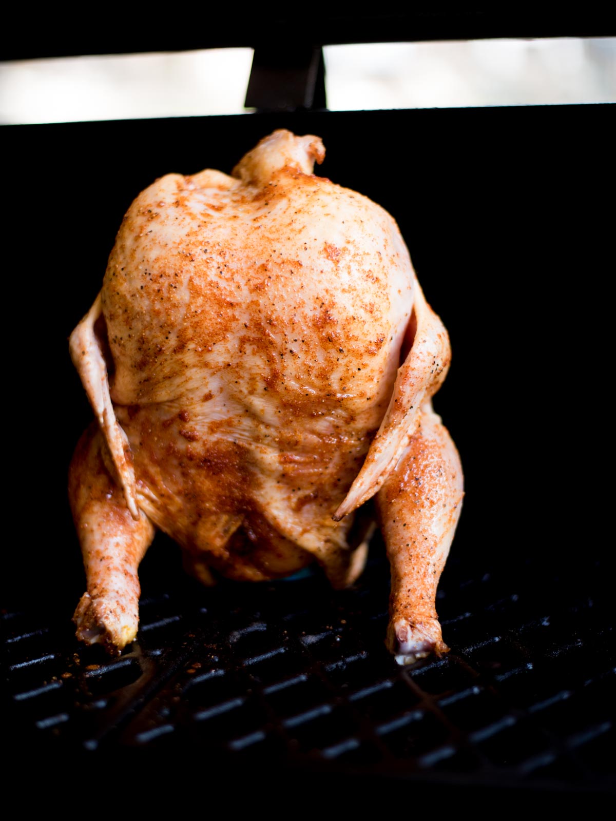 raw seasoned beer can chicken on a pellet grill standing up on a beer