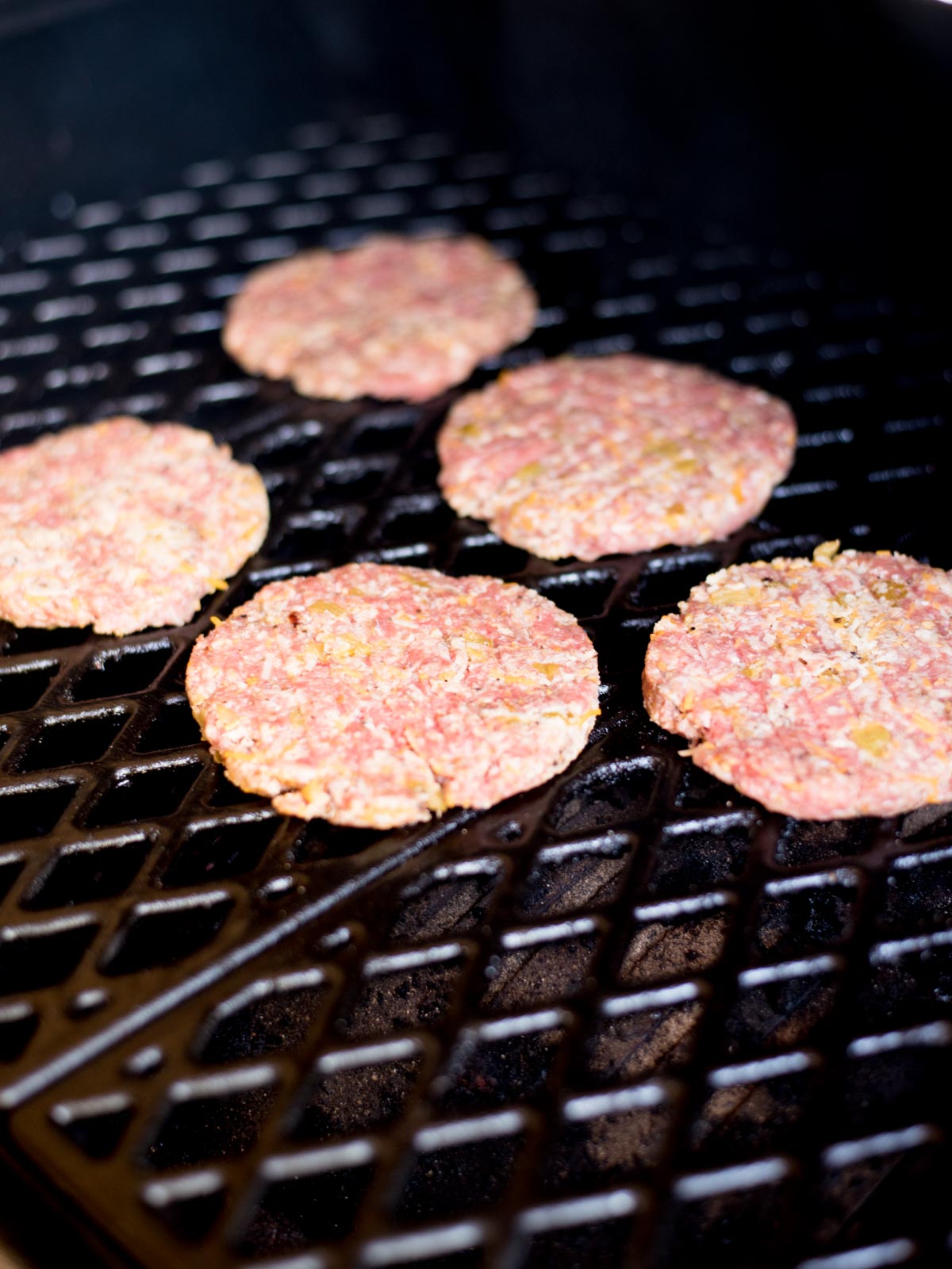 raw burgers on an electric smoker grate