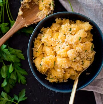 smoked macaroni and cheese in a blue bowl surrounded by parsley and a large spoon