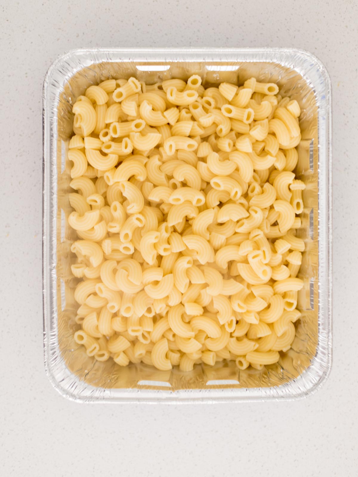 cooked elbow pasta added to a disposable cake pan