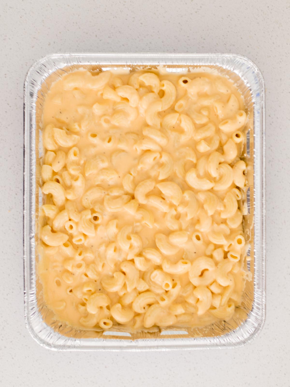 cheese sauce and cooked elbow pasta combined in disposable cake pan