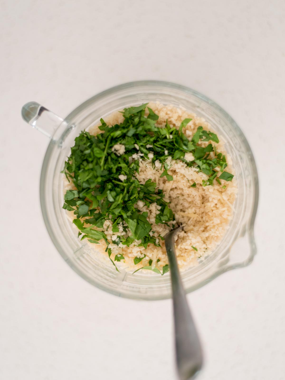 parsley added to the measuring cup with breadcrumbs, butter, and parmesan