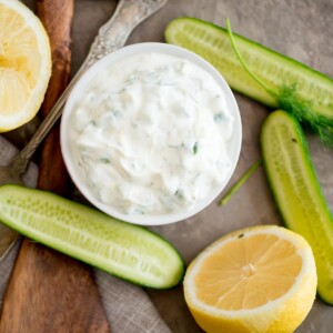 tzatziki sauce in a bowl surrounded by cucumbers and lemon